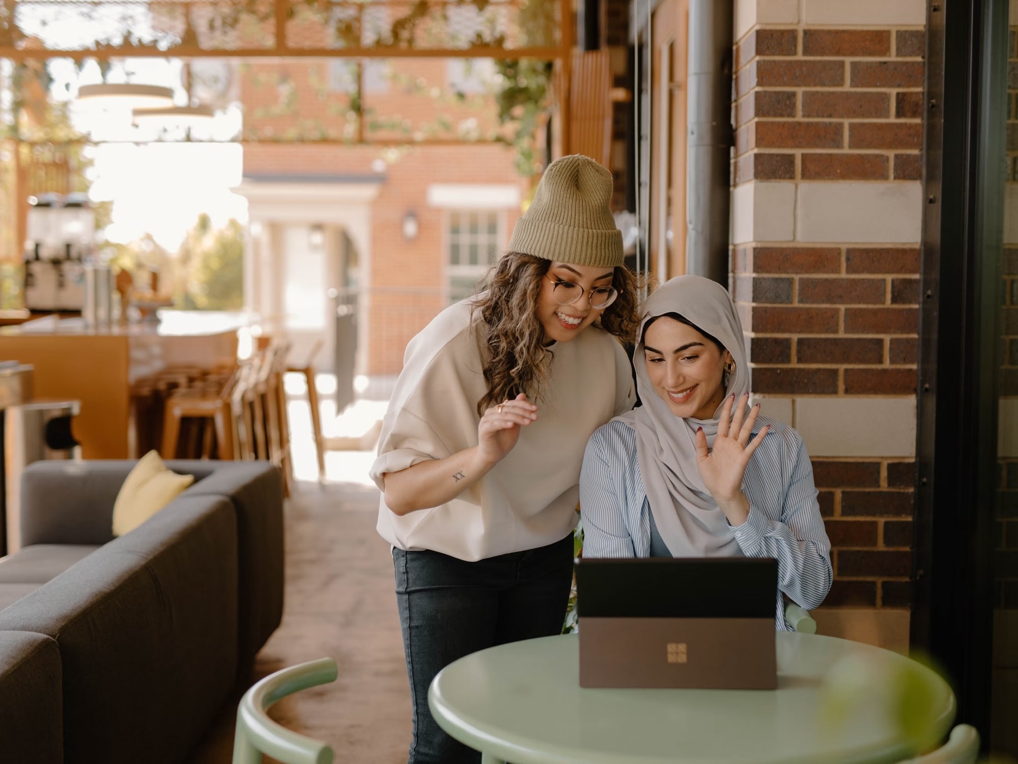 Two women in winter hats smiling at a laptop in a cozy cafe