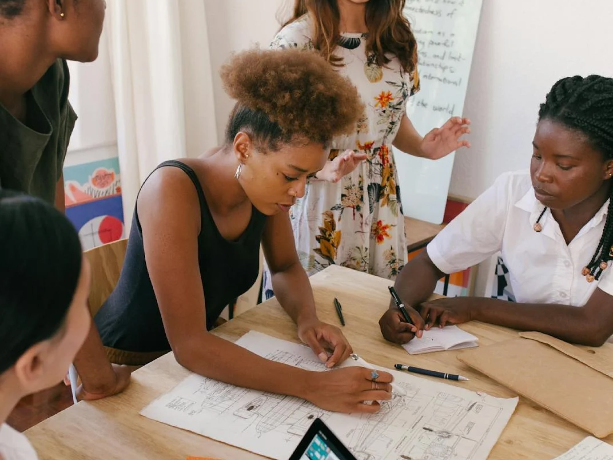 Group collaborating at a table, sketching plans on paper in a bright room