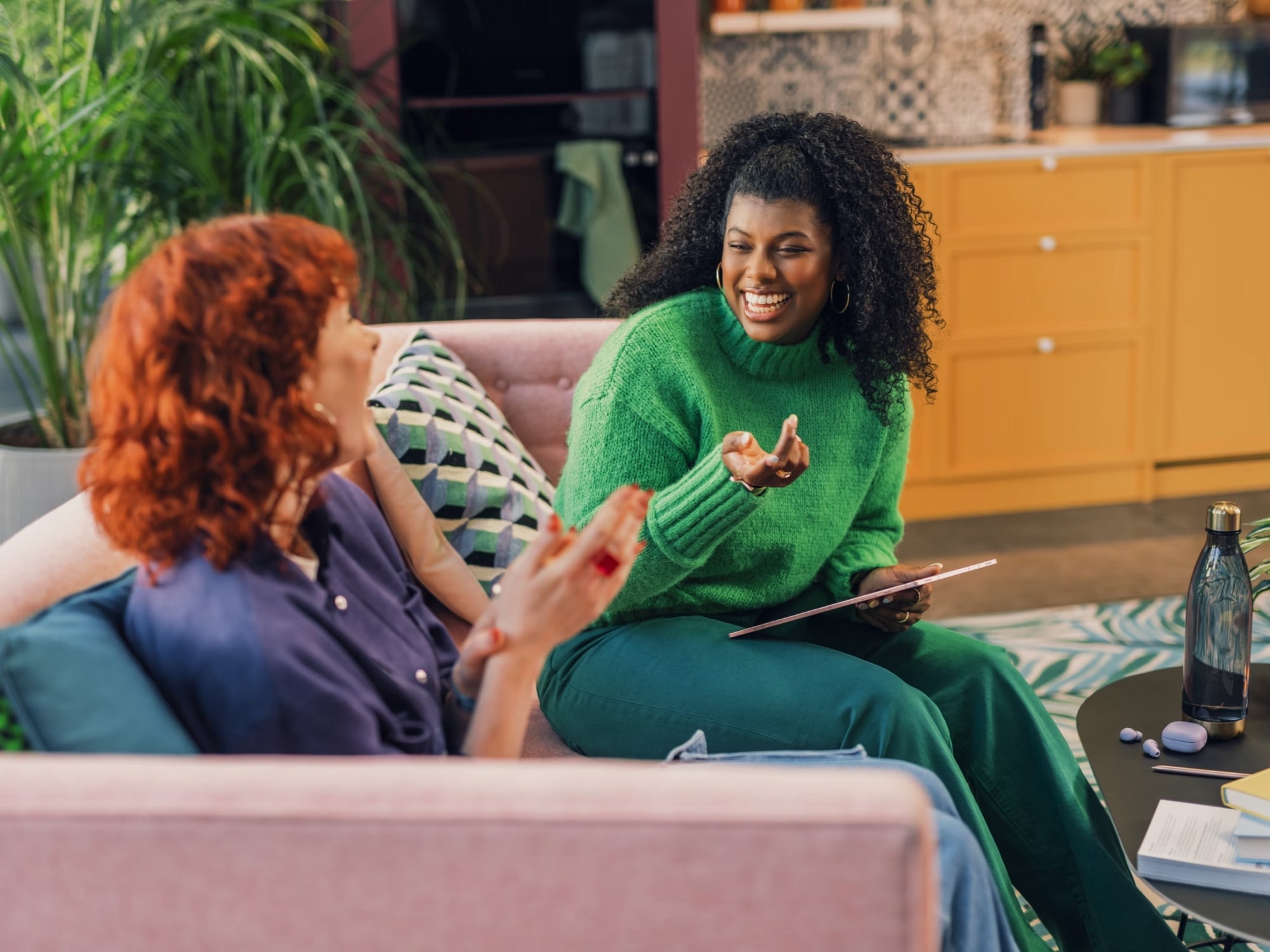 Two women chatting and smiling on a living room sofa with drinks on a coffee table