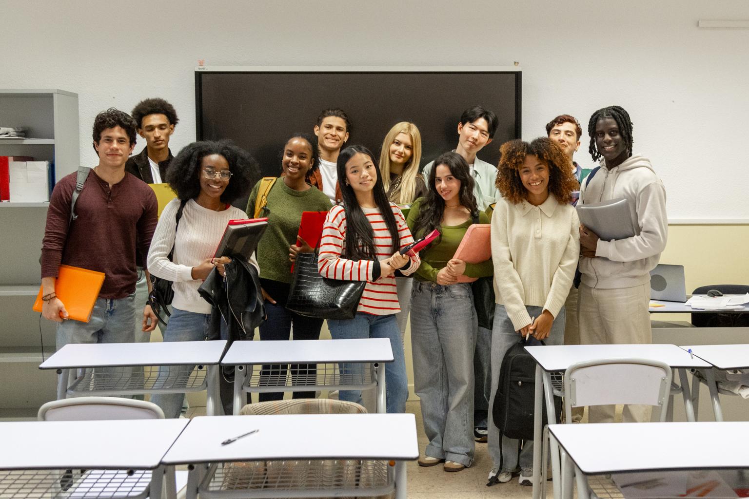 Group of students posing and smiling in a classroom with desks in front