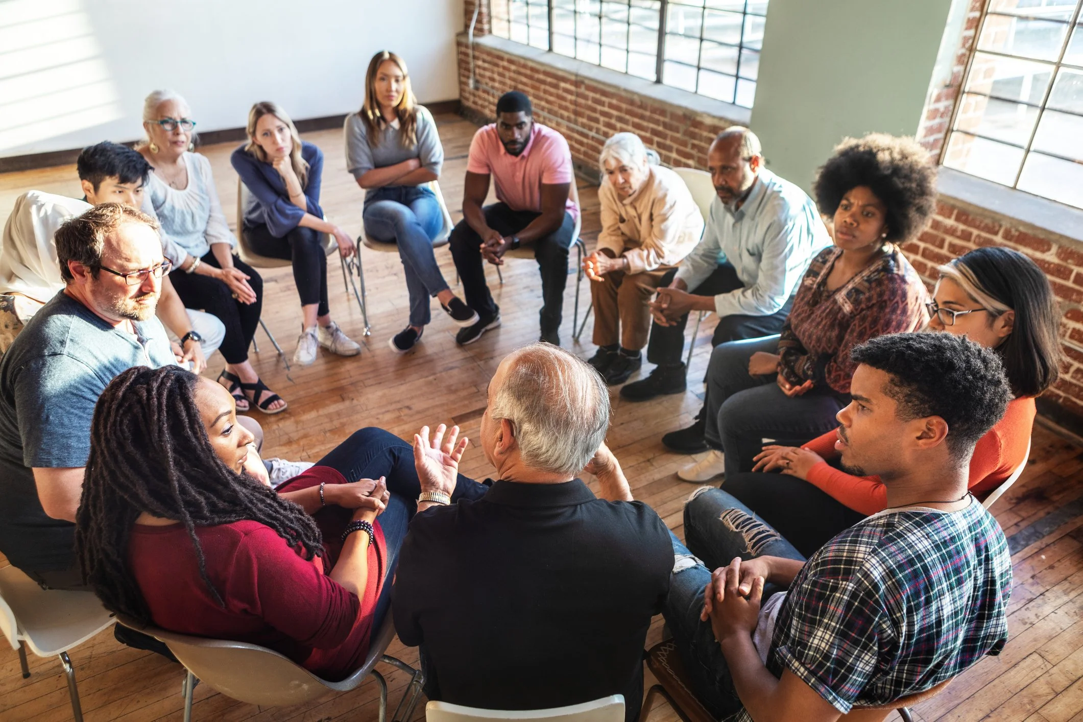 Support group in a bright room, people seated in a circle talking